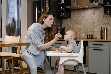 Paid parental leave policy is depicted with a mom feeds her toddler at home while on her maternity leave