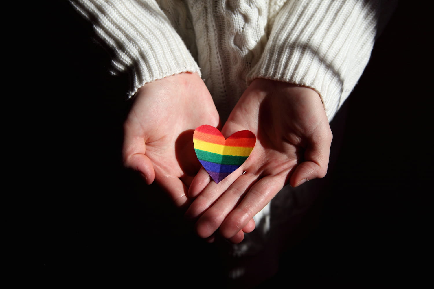  hands holding a a heart-shaped rainbow flag