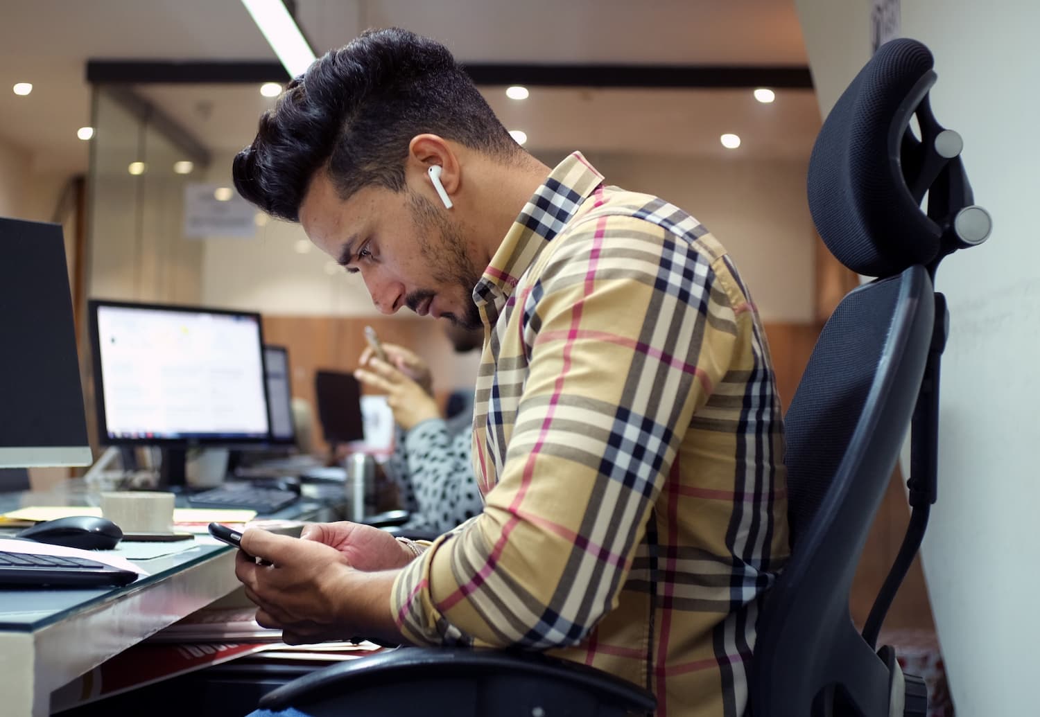  Employee wearing headphones looks at his phone while sitting at a desk