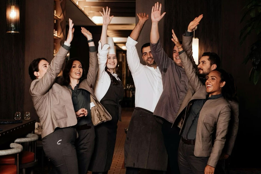 A group of people in a restaurant raising their hands in excitement and joy.
