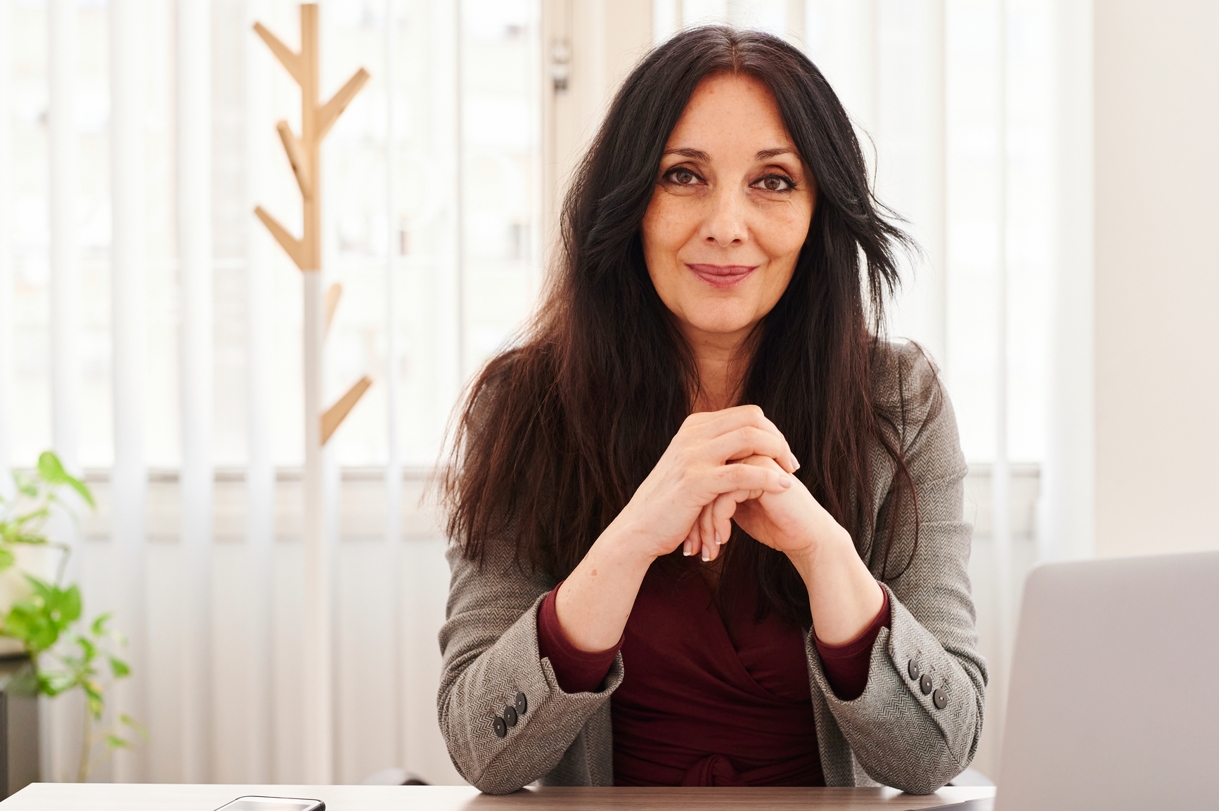  A mature woman sits at her desk with her hands clasped together in a confident manner