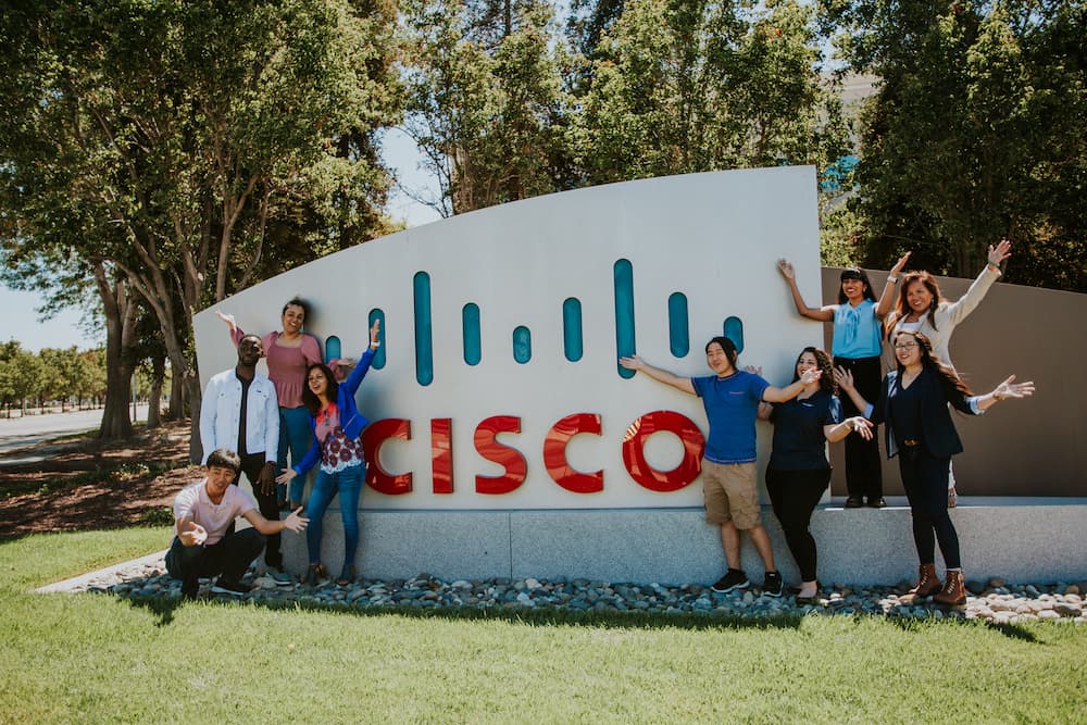  Cisco employees celebrating next to a Cisco sign