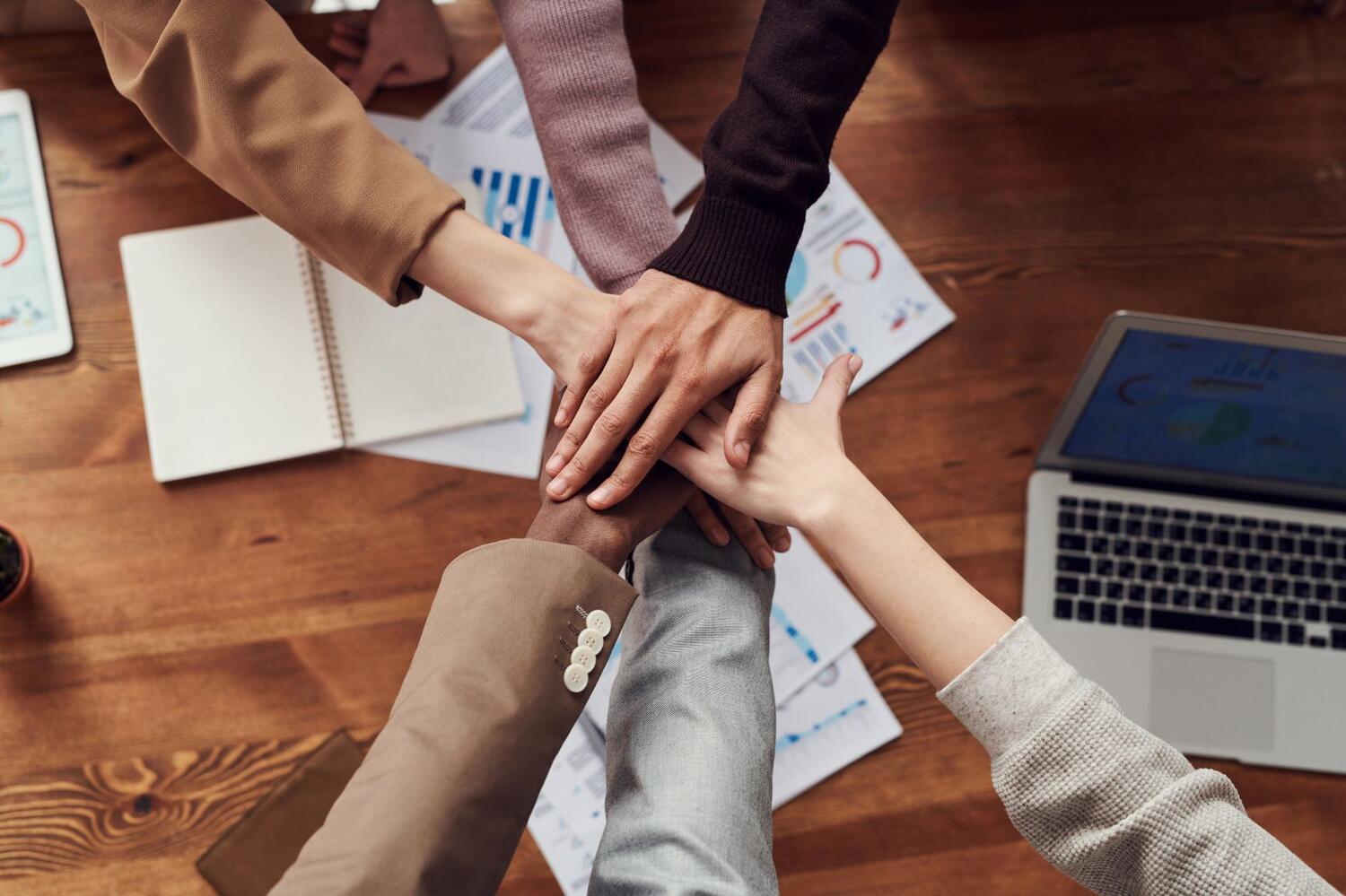  Diversity and inclusion in the workplace are exemplified by hands from different ethnic groups overlaping each other in a group high five.