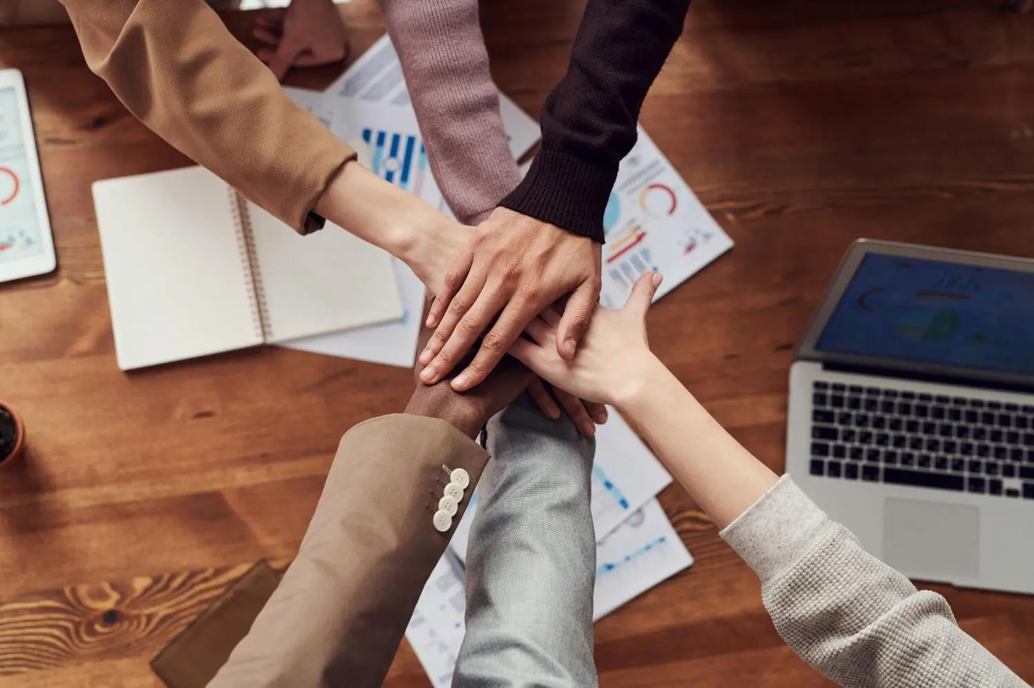  Diversity and inclusion in the workplace are exemplified by hands from different ethnic groups overlaping each other in a group high five.