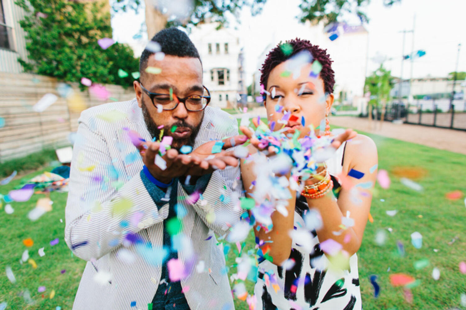  Employee recognition is depicted with two employees dressed smart for an awards event blow confetti in a celebratory fashion