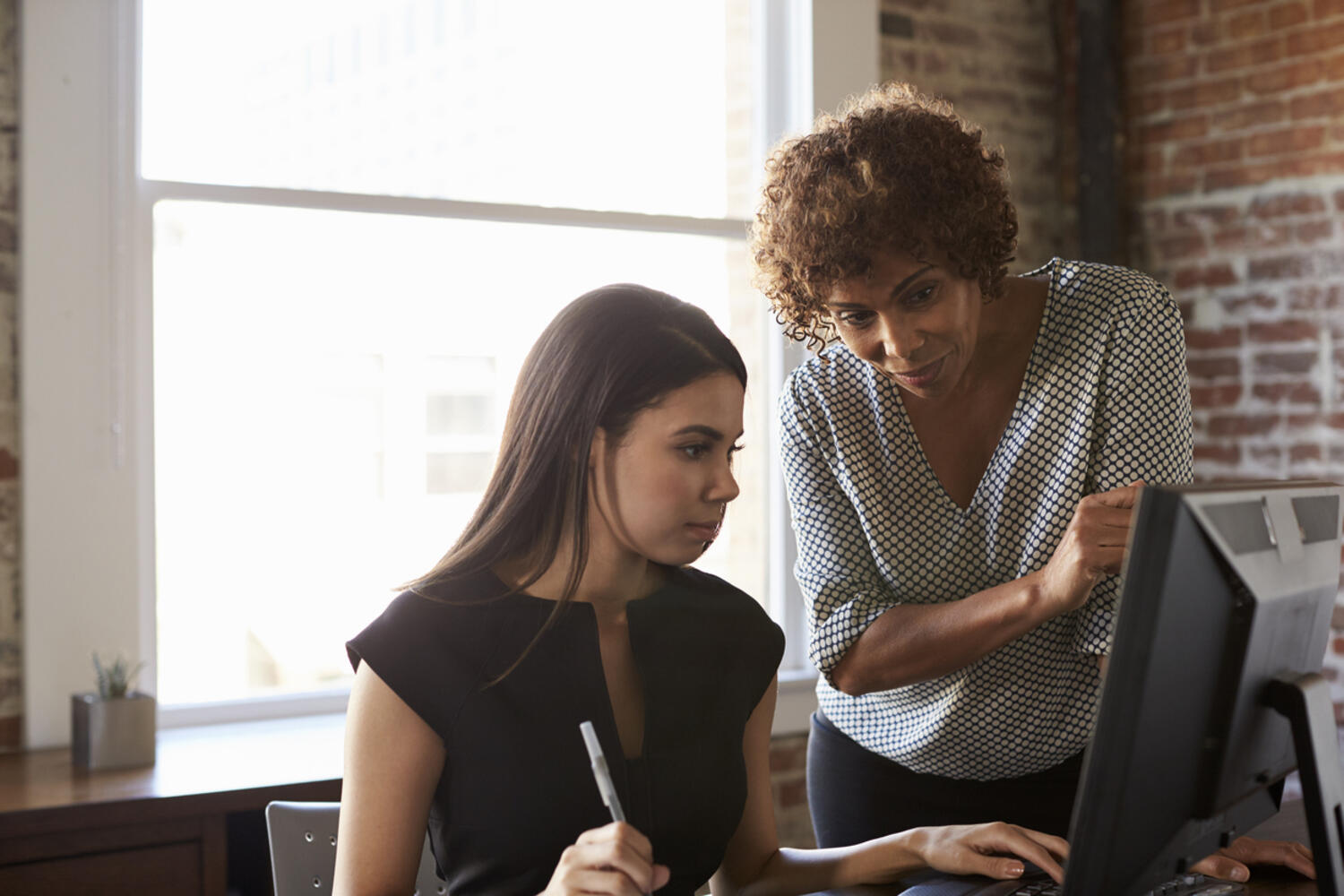  Manager effectiveness is exemplified by a manager looking over the shoulder of an employee while the employee is at their desk.