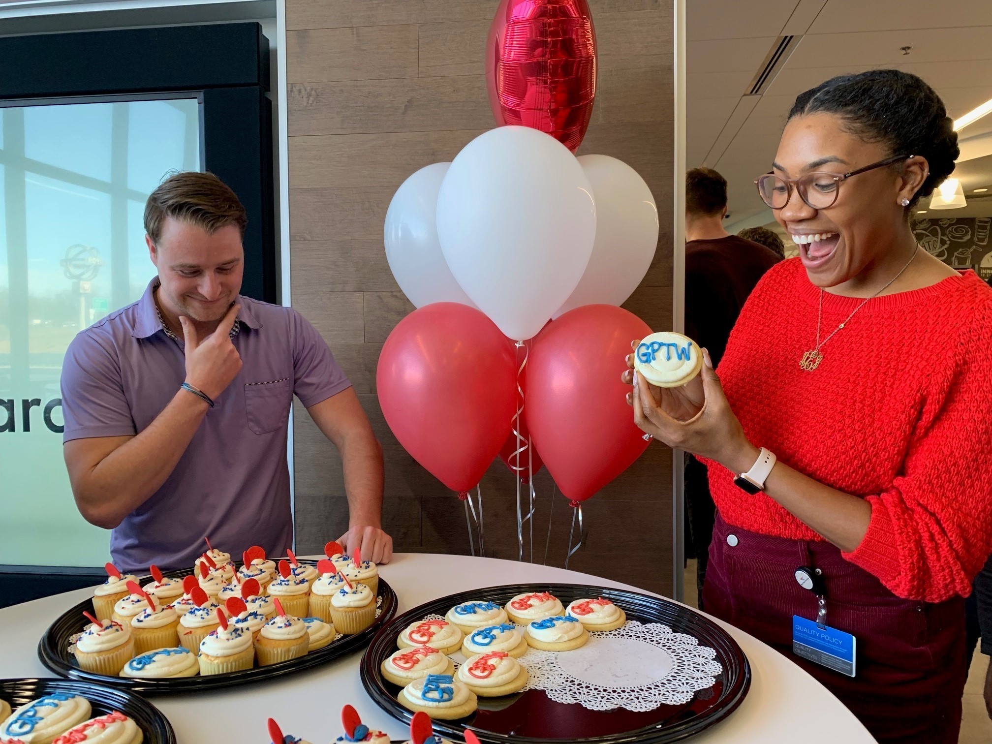  Promote your company culture award is depicted with two employees standing over a dessert stand. They're looking at cupcakes.