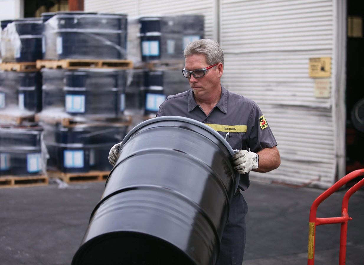 Man transporting an oil drum at a facility