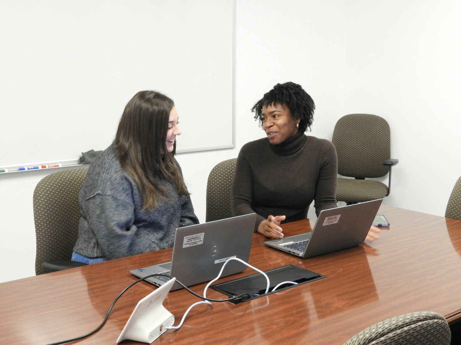 Two employees collaborate in a meeting room equipped with a Poly system and screens for seamless hybrid work.