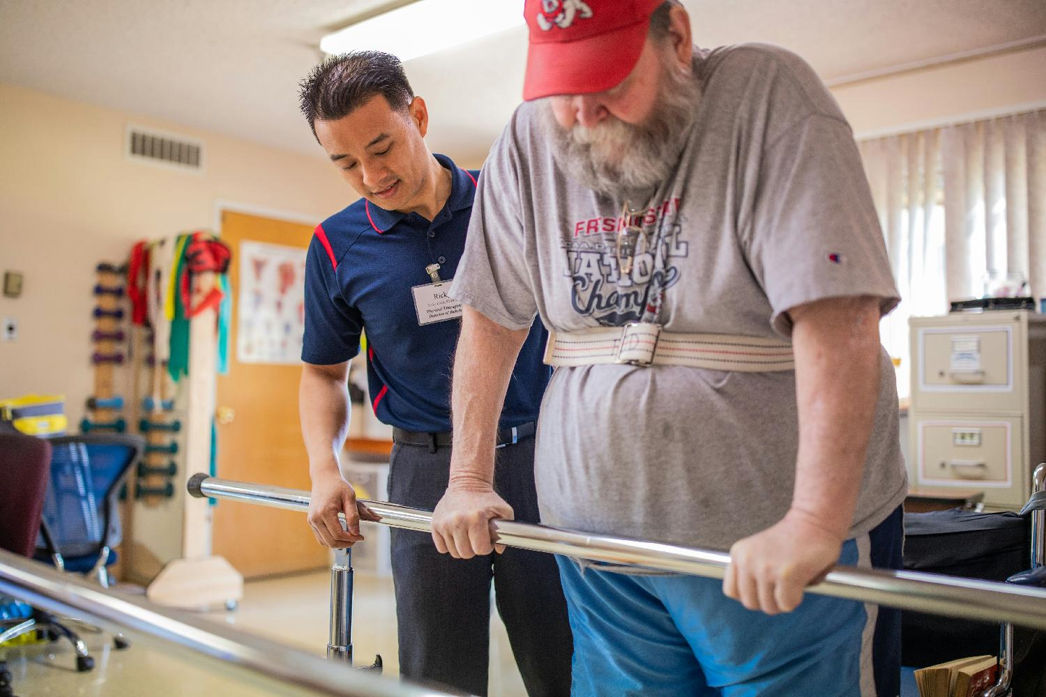 Eduro Healthcare physical therapist supports a patient using parallel bars to balance.
