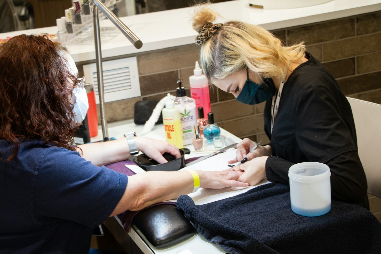 COSMETOLOGY STUDENT PRACTICING NAIL APPLICATION ON FELLOW STUDENT