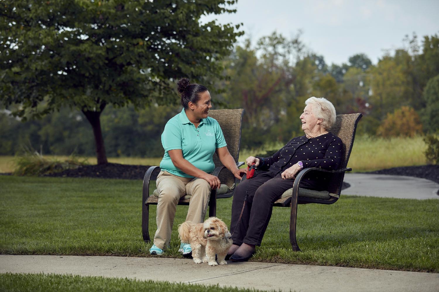 A caregiver and a resident enjoy a lively chat while sitting outdoors.