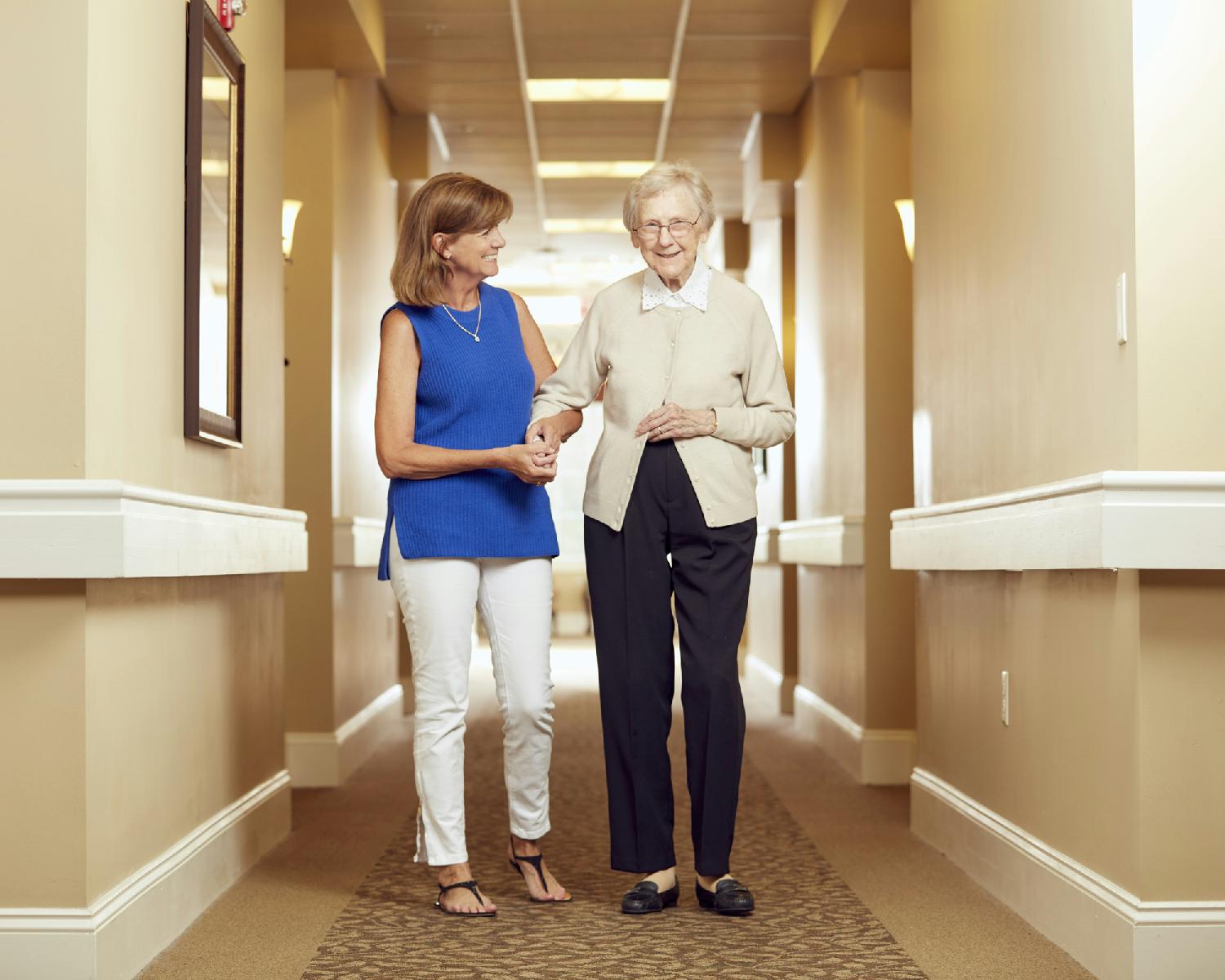A caregiver walks down the hallway with a resident.
