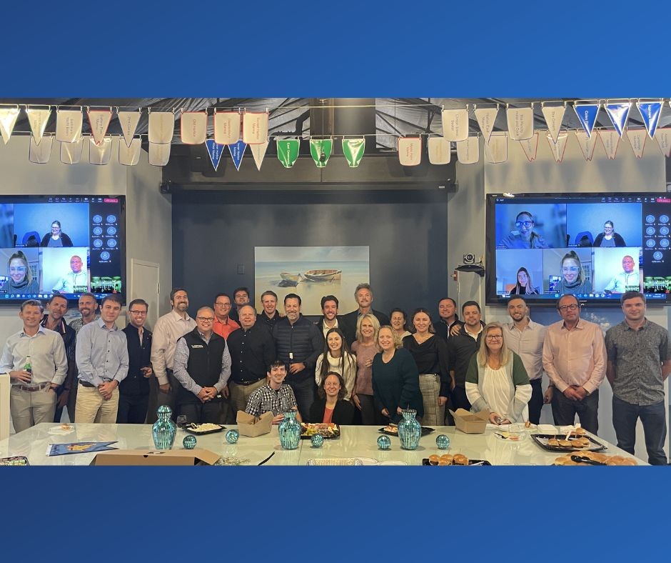 Group photo at the home office during a holiday party with virtual teammates in attendance via the monitors.