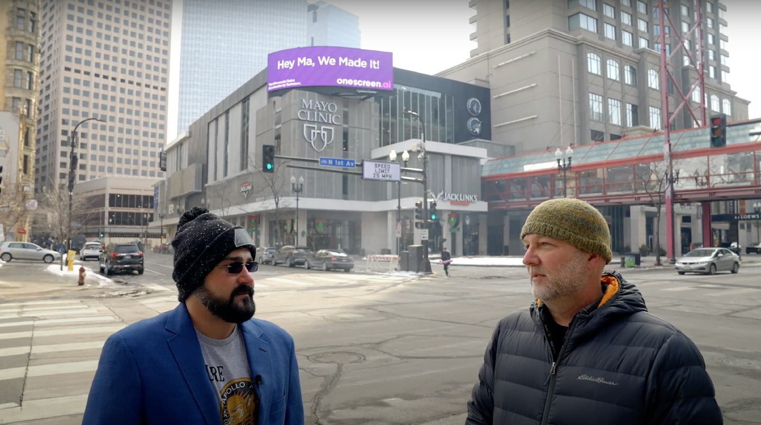 CEO Sampath Mallikarjunan and Chief Product Officer Dug Nichols in front of a OneScreen.ai billboard in Minneapolis