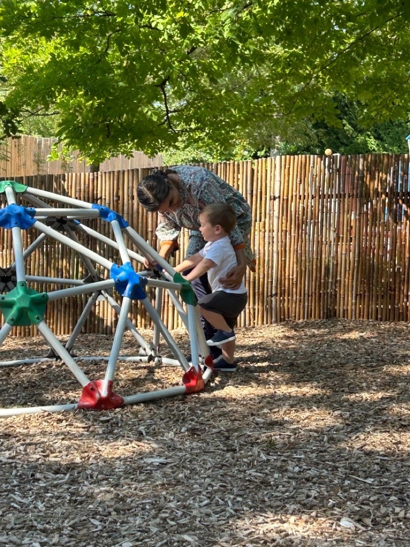A Toddler guide helping a child on the playground. 