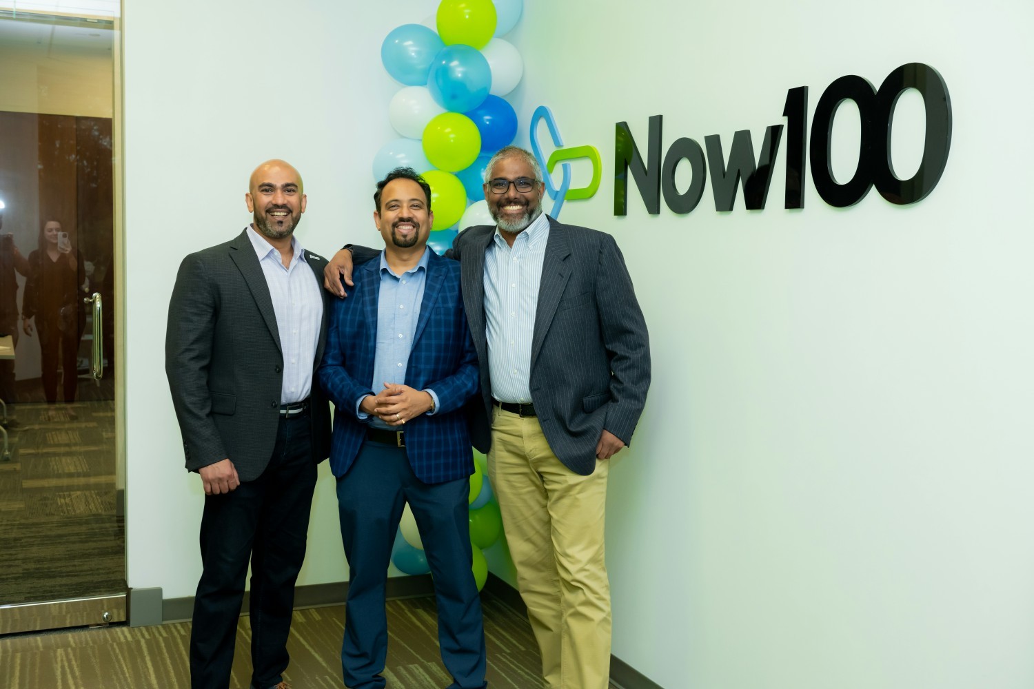 CEO, VP of Sales, and Director of Vendor Management stand in front of company logo during office inauguration.