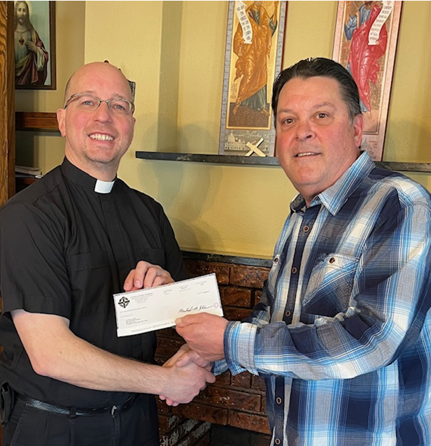 Member Advisor Scott Jones presenting a donation check to Father Theis