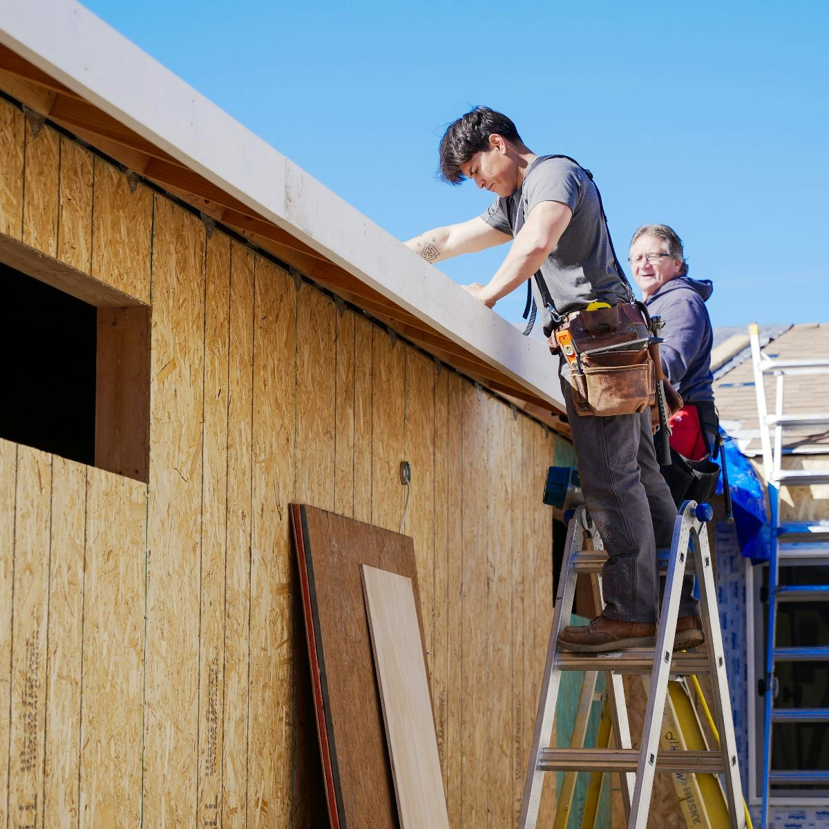 Crew members installing exterior components along the roofline of a residential build.