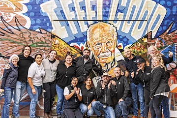 Employees at Nugget Market, No. 14 on the Fortune Best Workplaces in Retail™ list among large companies, stand in front of a graffiti mural of late chairman Gene Stille.
