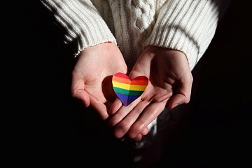 hands holding a a heart-shaped rainbow flag
