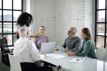 Managing a multigenerational workforce is depicted with a coworkers in a meeting room. They are a diverse group of people including young and older employees.  